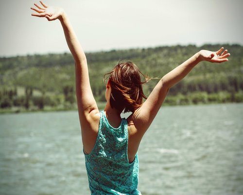 A person sitting at a desk and stretching their back gently with hands raised up high
