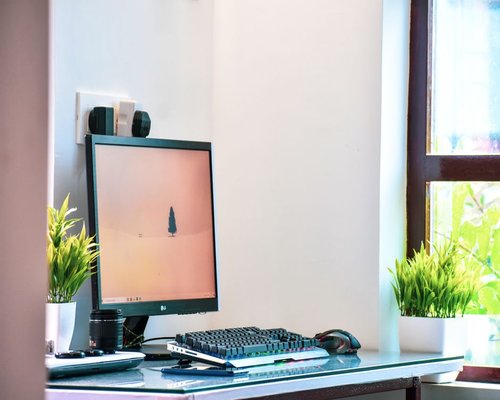 A bright home office corner with a small desk setup next to a large window showing green leaves
