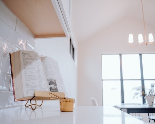 An open book on top of a table with a coffee cup in a brightly lit house room